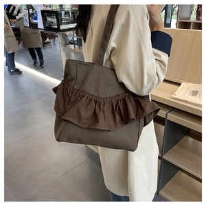 Detail of a dark brown canvas tote bag with layered ruffles on a stylish beige trench coat