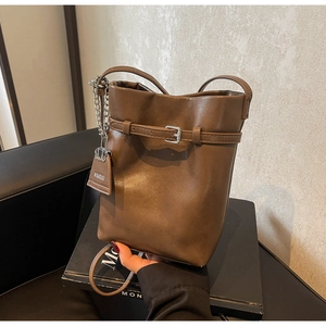 Detail of a brown leather bucket bag featuring silver buckle strap and metal chain strap