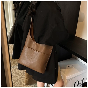 Close-up of a brown leather hobo shoulder bag featuring two front pockets and minimalist design
