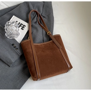 Chic brown faux suede tote bag with leather straps and gold buckle on a white fabric background