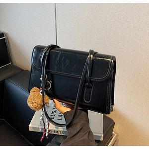 Detail of black glossy faux leather tote bag with cute teddy bear charm accessory