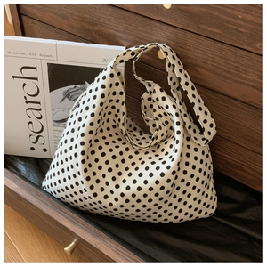 Detail of hobo bag in polka dot canvas with logo tag inside a wooden drawer