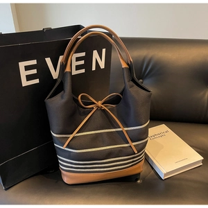 Detail of canvas tote bag showing striped pattern, bow tie, and leather base on sofa