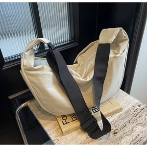 Close-up of beige crescent bag in nylon with adjustable black strap on marble surface