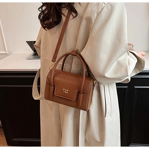 Detail of a brown leather crossbody bag with golden PAN TOR logo and smooth dual handles