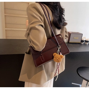 Detail of burgundy patent leather shoulder bag with plush bear and striped ribbon