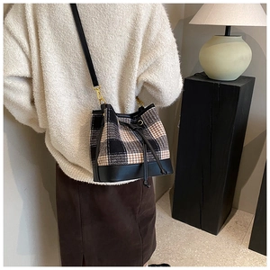 Détail d'un sac seau à carreaux avec base en cuir noir et finitions dorées chic