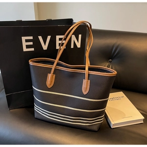 Detail of canvas tote bag with brown leather handles and white stripe decor on a sofa