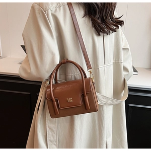 Deep brown leather mini square crossbody bag worn by a model in a stylish trench coat