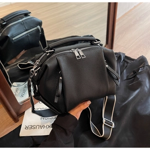 Detail of black pebbled leather crossbody bag with pleated corners and silver zippers