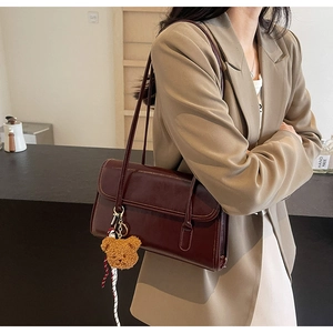 Detail of dark red vintage shoulder bag with plush bear charm worn with beige blazer