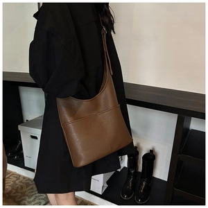 Detailed view of a dark brown crescent shoulder bag worn with an oversized coat