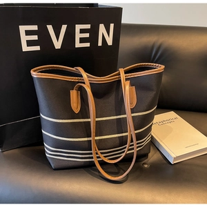 Detail of striped canvas tote bag with brown faux leather handles on a leather sofa