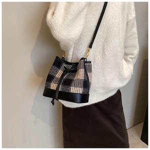Détail d'un sac seau en pied-de-poule avec bordure en cuir sur une tenue d'automne