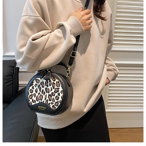 Detail of round leopard print crossbody bag featuring golden logo and black leather trim