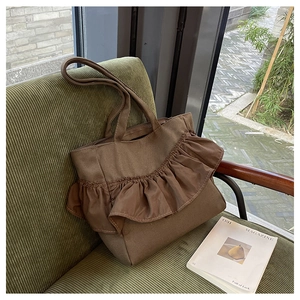 Detail of coffee canvas tote bag with silk ruffles resting on green corduroy chair