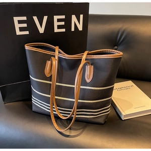Close-up of striped canvas tote bag with brown leather handles on a leather sofa