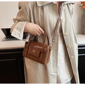 Close-up of a brown glossy leather handbag with gold PAN TOR logo and shoulder strap