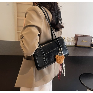 Detail of a shiny black faux leather shoulder bag with a cute plush bear pendant