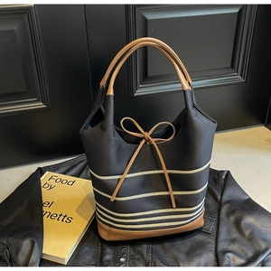 Detail of striped canvas tote with brown leather handles and decorative bow on top