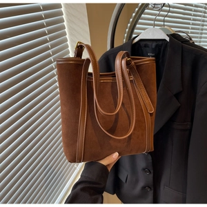 Detailed view of brown suede bucket bag with leather trim and gold metal buckles