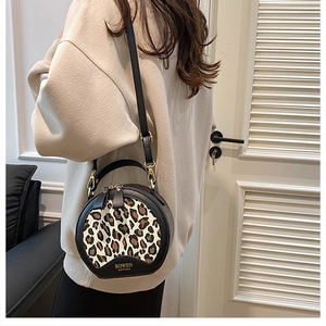 Detailed close-up of leopard print panel and gold logo on black round crossbody bag