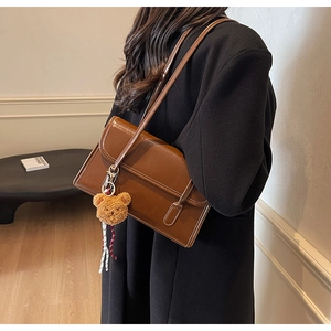 Detail of a dark brown faux leather underarm bag with a magnetic flap and cute bear charm