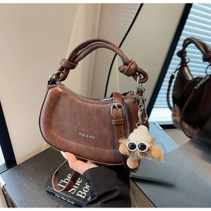 Detail der dunkelbraunen Satteltasche mit Knotengriffen, Logo und süßem Plüsch-Anhänger