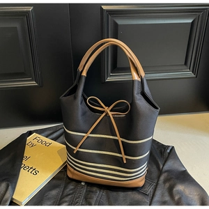 Detail of striped canvas tote bag featuring brown leather trim and bow knot accent