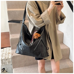 Dettaglio della borsa tote in pelle nera opaca con ciondolo a orsetto e cerniere decorative