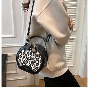 Detail shot of a round leopard print crossbody bag with gold zipper and brand logo