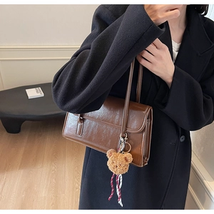 Detail of dark brown faux leather shoulder bag featuring a cute plush bear charm