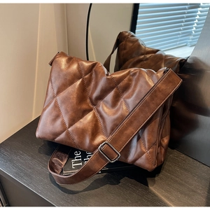 Detailed close-up of brown quilted faux leather cross-body bag with wide strap and metal buckle