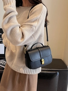 Elegant black lychee grain leather crossbody bag with gold buckle on a beige knit sweater