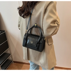 Detail shot of a black PU leather square handbag with golden PAN 'TOR logo and strap