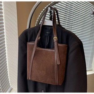 Detail of dark brown suede tote bag with leather trim and gold buckles on a blazer