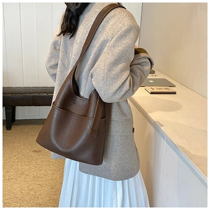 Detail view of a vintage dark brown leather tote bag worn with a casual gray blazer