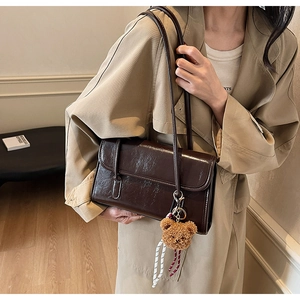 Detail of dark brown vintage faux leather shoulder bag with cute plush bear keychain