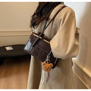 Detail of dark brown patent leather shoulder bag with a cute plush bear keychain