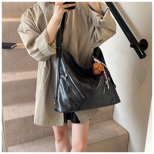 Dettaglio borsa hobo in similpelle nera con tasche a zip e ciondolo a forma di orso