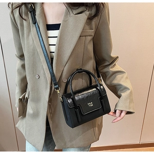 Detail of black mini leather handbag with round handle and gold hardware on brown suit