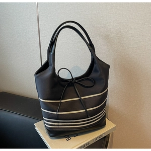 Detail of striped canvas tote bag with black leather bow accent on a book prop