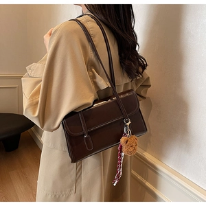 Detail view of deep coffee shoulder bag with plush bear charm on a trench coat