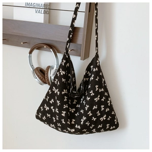 Close-up of black canvas tote bag featuring white bow patterns and long shoulder strap