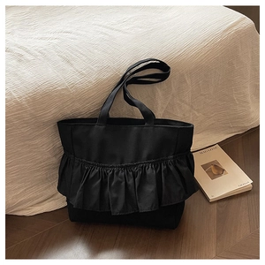 Detail of a black canvas tote bag featuring stylish ruffle pleats and dual flat handles