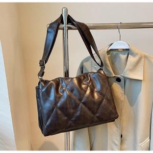 Close-up of a dark brown quilted crossbody bag with glossy texture and wide strap