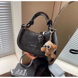 Detail einer schwarzen Halbmond-Handtasche mit Knotengriff und Plüschtier-Anhänger
