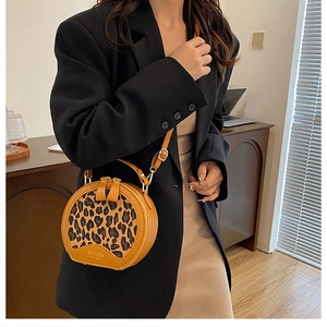 Close-up of a leopard print round bag styled with a black blazer and beige dress