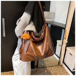 Dettaglio borsa tote hobo marrone grande con cerniere diagonali e ciondolo a orsetto