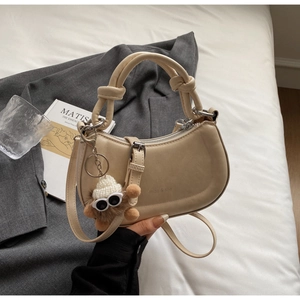 Details der beigen Satteltasche mit Knotengriff, Plüschbär-Anhänger und matter Textur